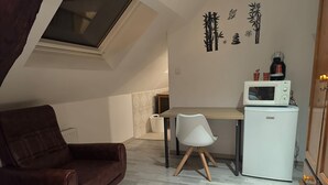 A cozy room with a brown leather chair, a white chair, a small desk, a white refrigerator, and a microwave.