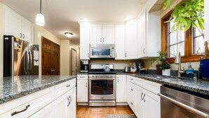 A kitchen with white cabinets, stainless steel appliances, granite countertops, and a wooden floor. - The Ultimate Irish Getaway | 1.5 Miles from Campus (South Bend)