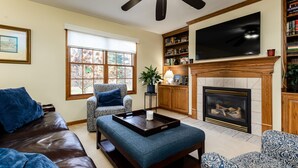A living room with a sofa, ottoman, fireplace, television, and bookshelves. - The Ultimate Irish Getaway | 1.5 Miles from Campus (South Bend)