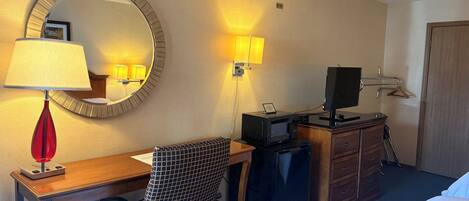 A hotel room with a desk, chair, bed, television, and a mirror.