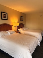 Habitación de hotel con dos camas, una mesita de noche con lámpara y cuadros en la pared.