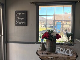 Una habitación con ventana, un cartel que dice 'Gratitude Changes Everything', un florero con flores y un letrero que dice 'HOGAR' sobre una mesa.