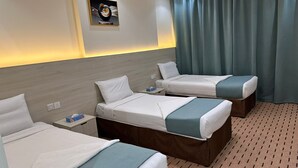 Una habitación de hotel con tres camas, una mesita de noche, una obra de arte colgada en la pared y una cortina.