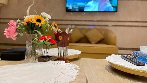 Una sala de estar con televisión, un florero con flores, un sofá y una mesa con un control remoto.