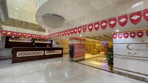 Un vestíbulo de hotel con mostrador de recepción, banderines decorativos, una araña y una pared grande con un símbolo de luna creciente.