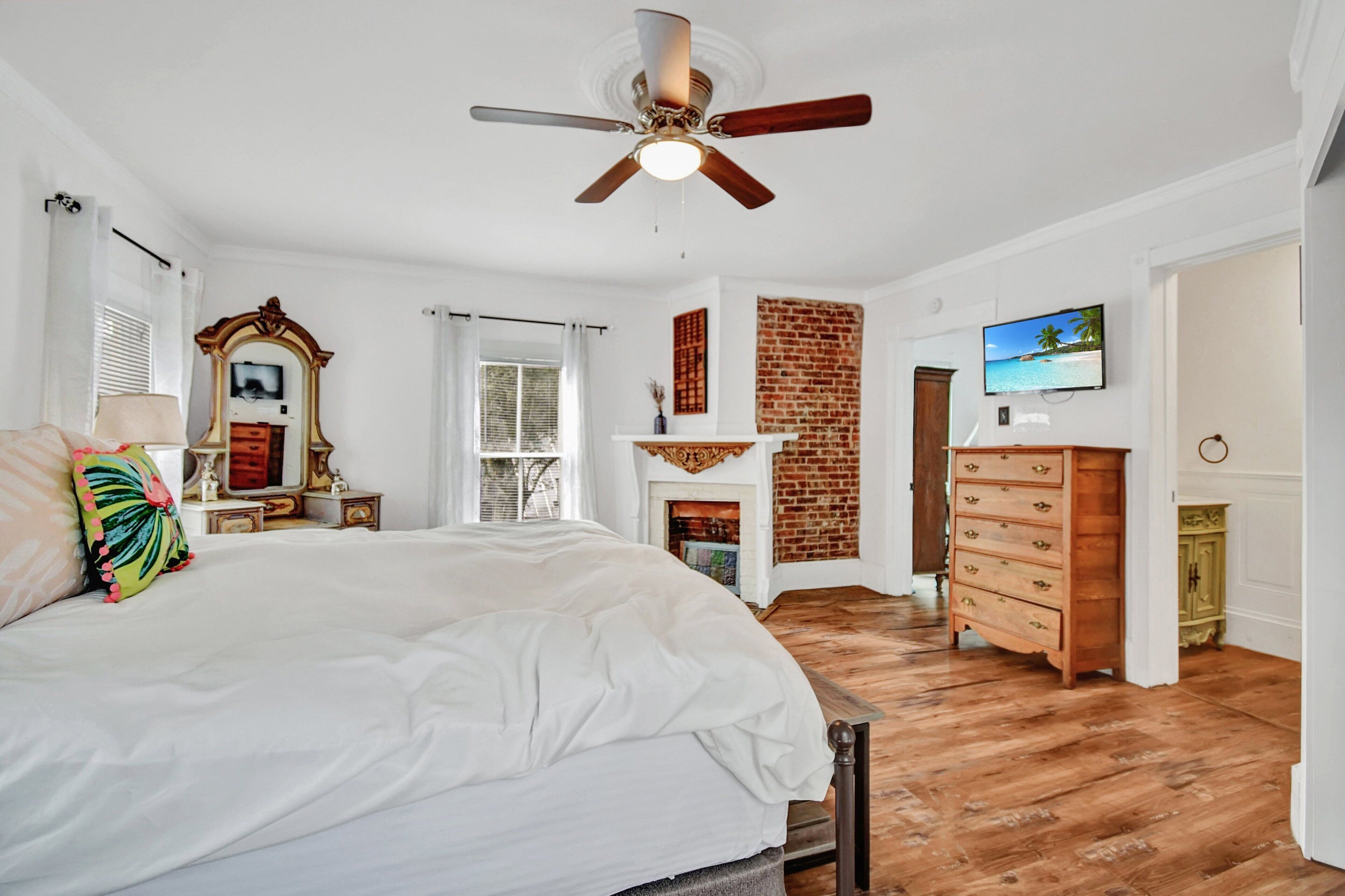 A bedroom with a large bed, a ceiling fan, a fireplace, a TV, and a brick wall.