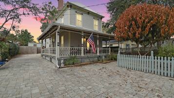 Uma casa de dois andares com varanda, uma bandeira americana e cerca branca de piquete.