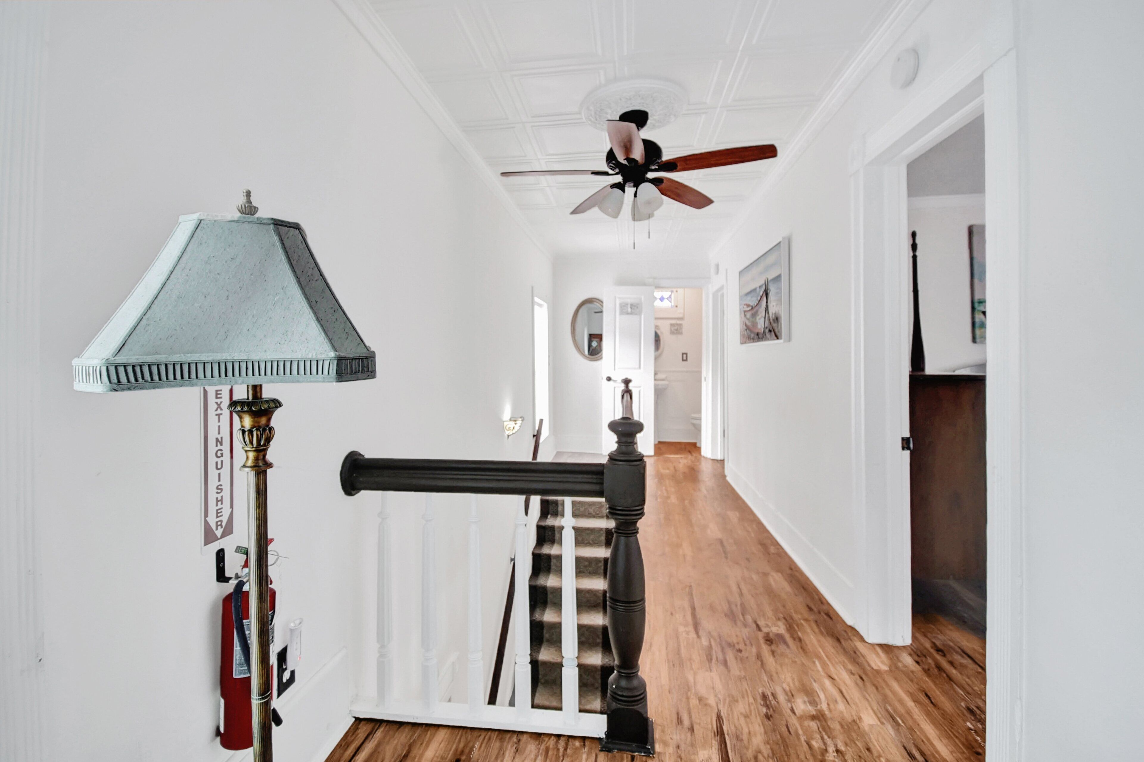 A hallway with a ceiling fan, a staircase with a banister, and a fire extinguisher on the wall.
