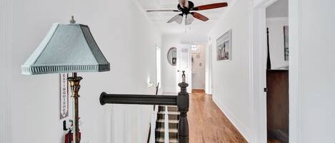 A hallway with a ceiling fan, a staircase with a banister, and a fire extinguisher on the wall.