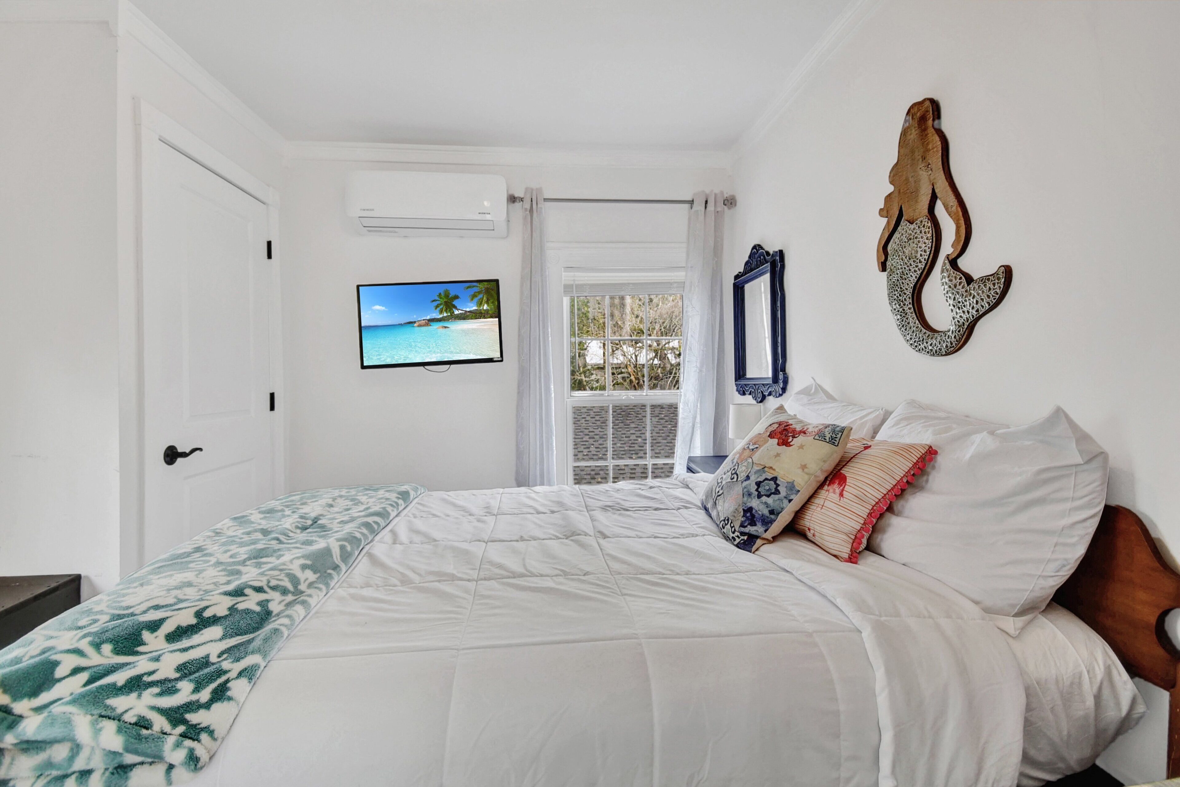Une chambre à coucher comprenant un lit, une télévision, une fenêtre avec des rideaux et un miroir fixé au mur.