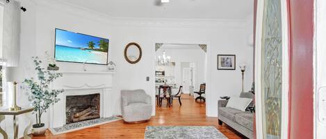 Un salon avec une cheminée, un téléviseur, un ventilateur de plafond et un coin repas à l’arrière-plan.