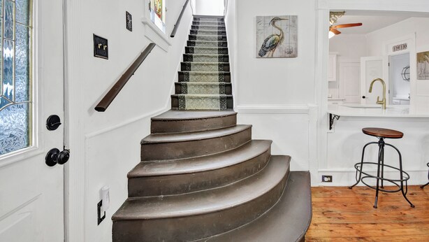 Una escalera con alfombra estampada, barandilla de madera y una lámpara fijada a la pared.