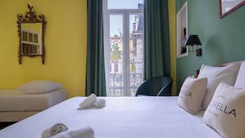 A hotel room with a bed, two bedside tables, a mirror, a window with curtains, and a view of buildings outside.