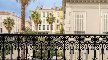 A balcony with a wrought iron railing, overlooking a street with palm trees and buildings.