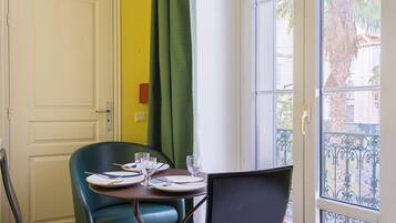 A room with a dining table set for two, a chair, a bed, an air conditioning unit, and a window with a view of palm trees.