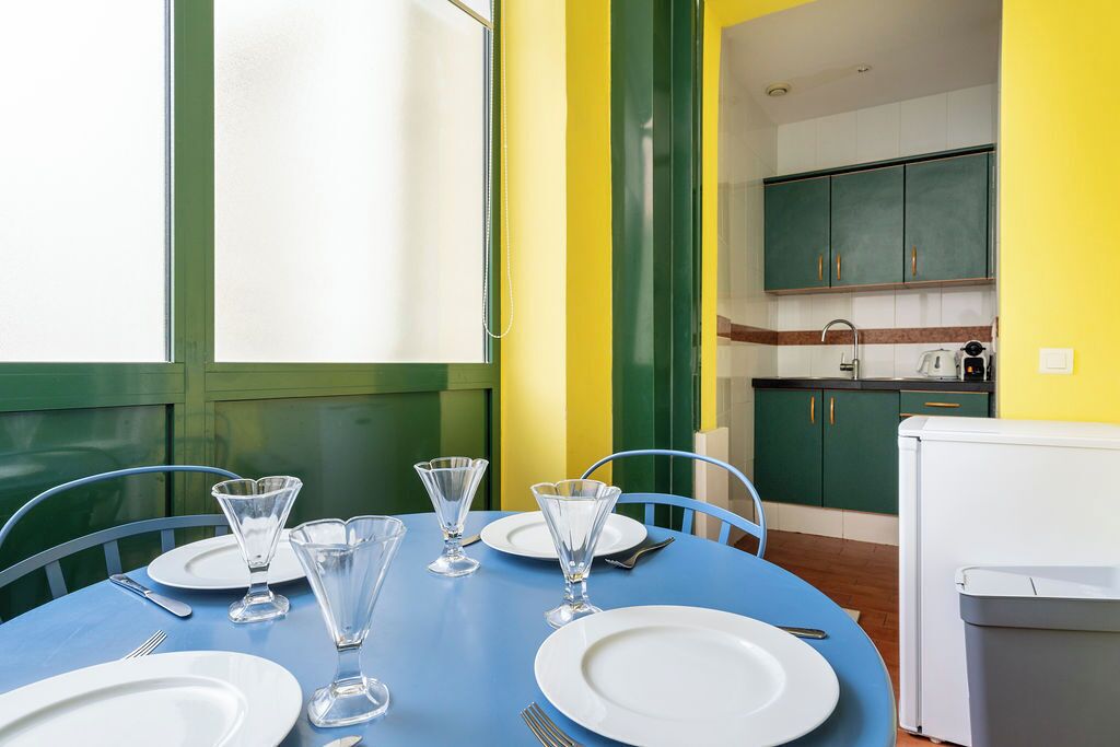 A dining table set with plates, glasses, and cutlery, with a kitchen in the background.