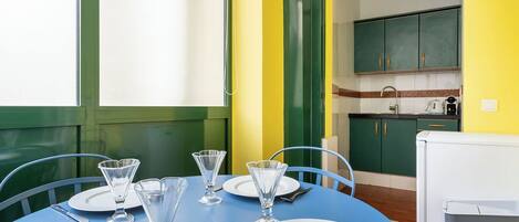 A dining table set with plates, glasses, and cutlery, with a kitchen in the background.