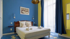 Un dormitori amb un llit doble, dues taules de nit, una làmpada penjada a la paret i una finestra amb cortines blaves.