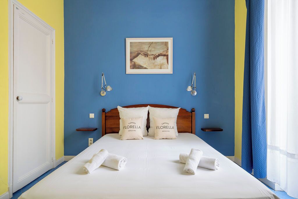 Une chambre d’hôtel avec un lit, deux oreillers, un tableau encadré, des lampes de chevet et une porte.