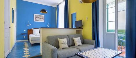 Una habitación con un sofá gris, una mesita, una cama y un televisor.