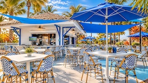 An outdoor dining area with tables and chairs, umbrellas, and a pool.