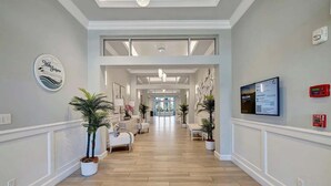 A hotel hallway with a wooden floor, white walls, and a reception desk with a television.