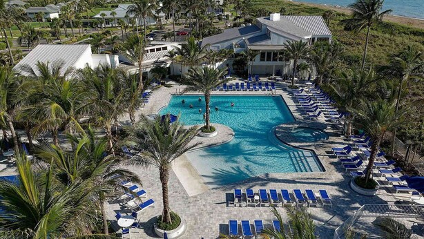A resort with a large pool, palm trees, and beach views.