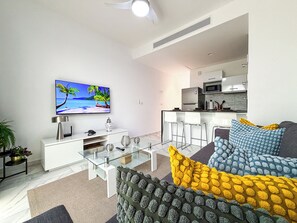 A modern living room with a flat-screen TV, a glass coffee table, and a sofa with patterned cushions. - Resort-Style Penthouse with Breathtaking Views (Punta Cana)