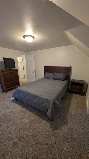 Un dormitorio con cama, cómoda, mesita de noche y televisor sobre la cómoda.