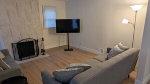 Un salon moderne avec un canapé gris, un téléviseur à écran plat, une cheminée et un lampadaire.