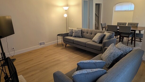 Un salon moderne avec un canapé gris, une lampe sur pied et un coin repas comprenant une table et des chaises.