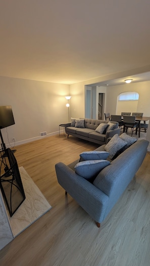 Una sala de estar moderna con un sofá gris, una lámpara de pie y un comedor con una mesa y sillas.