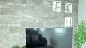Un salon moderne doté d’un grand téléviseur à écran plat, d’un meuble de rangement en bois et d’un mur en pierre grise.