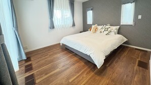 Une chambre avec un grand lit, deux fenêtres avec des rideaux, un mur gris à texture et un plancher en bois.