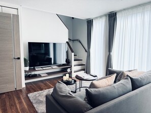 A modern living room with a flat-screen TV, a sofa, a coffee table, and a staircase. - Akikawa Koshi 6 | 15 min to TSMC | Entire 5LDK House | Up to 7 Guests (合志市)