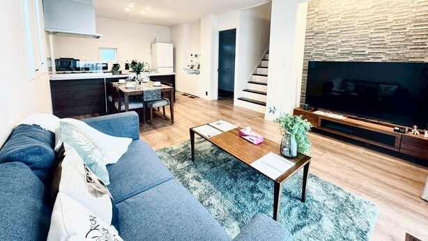 Una sala de estar moderna con un sofá, una mesa de centro y un televisor. Se aprecia una cocina al fondo con un comedor.