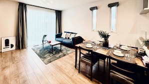 Una sala moderna con sofá, mesa de comedor para cuatro personas y un amplio ventanal con cortinas.
