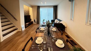 Un comedor con una mesa de madera dispuesta para cuatro, un televisor al fondo y una escalera a la izquierda.