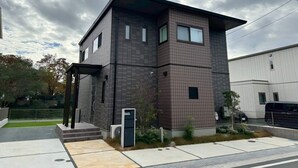 A modern two-story building with a flat roof, a covered entrance, and a small garden area. - Akikawa Koshi 7 | 15 min to TSMC | Entire 4LDK House | Up to 7 Guests (合志市)