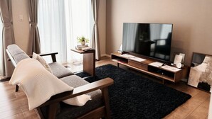 A modern living room with a sofa, TV, and a small side table with a plant. - Akikawa Koshi 7 | 15 min to TSMC | Entire 4LDK House | Up to 7 Guests (合志市)
