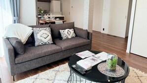A modern living room with a grey sofa, a round coffee table, and a kitchen in the background. - Akikawa Koshi 5 | 15 min to TSMC | Entire 3LDK House | Up to 4 Guests (合志市)