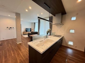 A modern kitchen with a central island, built-in appliances, and a dining area with a sofa and TV. - Akikawa Koshi 5 | 15 min to TSMC | Entire 3LDK House | Up to 4 Guests (合志市)