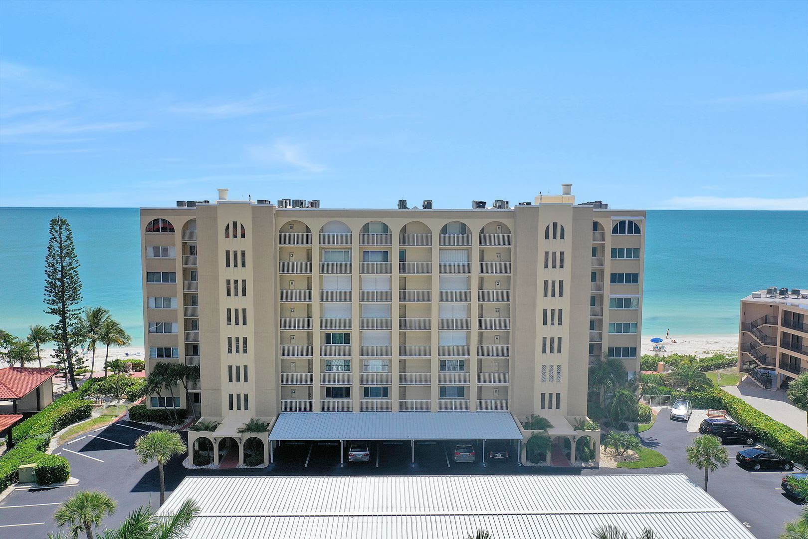 Ein mehrstöckiges Hotel mit Innenhof, Parkplatz und Blick auf den Strand.