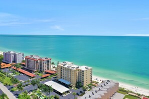 A coastal hotel with multiple buildings, a parking lot, and a beach view. - Beachfront Living in a Stunning Condo (Bonita Springs)