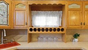 A kitchen with wooden cabinets, a red sink, and a window with a white curtain. - All American Style / 18 min to Manhattan (Carlstadt)