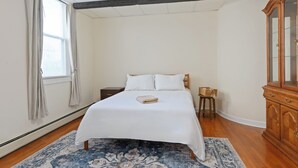A bedroom with a large bed, a wooden cabinet, and a window with curtains. - All American Style / 18 min to Manhattan (Carlstadt)