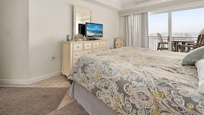 Une chambre d’hôtel avec un grand lit, une commode avec un téléviseur, un balcon avec vue et un ventilateur de plafond.