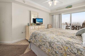Ein Hotelzimmer mit einem großen Bett, einem Schminktisch mit Fernseher, einem Balkon mit Blick und einem Deckenventilator.