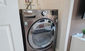 A front-loading LG direct drive washing machine in a laundry room with a white door and a small plant on a white counter. - Caliber / 2 King Beds / Elevator / 2 Ensuite / W/D (Philadelphia)
