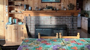 Eine gemütliche Küche mit Holzausstattung, einem Kamin aus Ziegelsteinen und einem Essbereich mit einem blumigen Tischläufer.